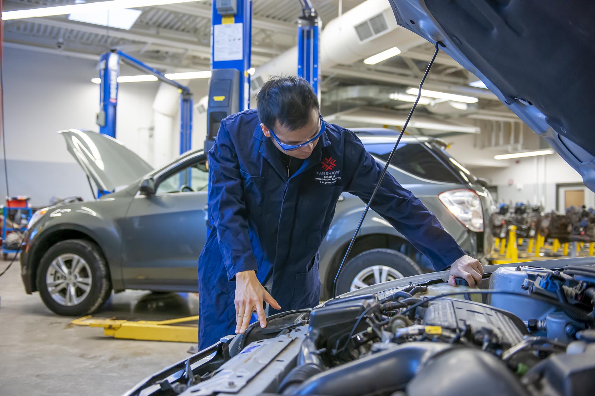 Student in automotive lab, looking under hood of car