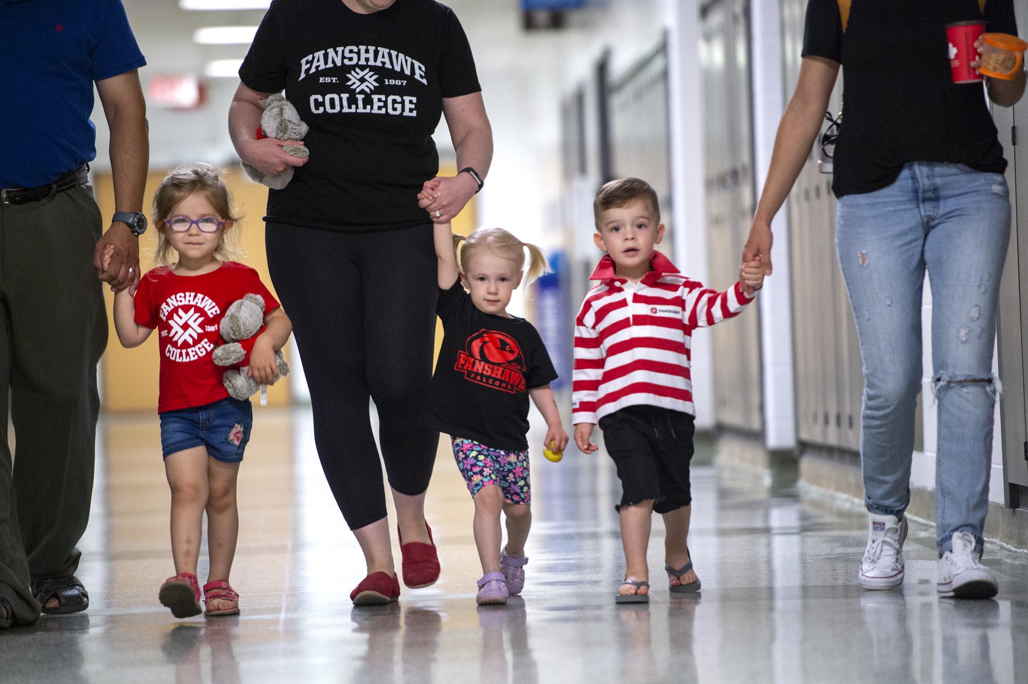 Three children walking down hallway, holding hands with three adults