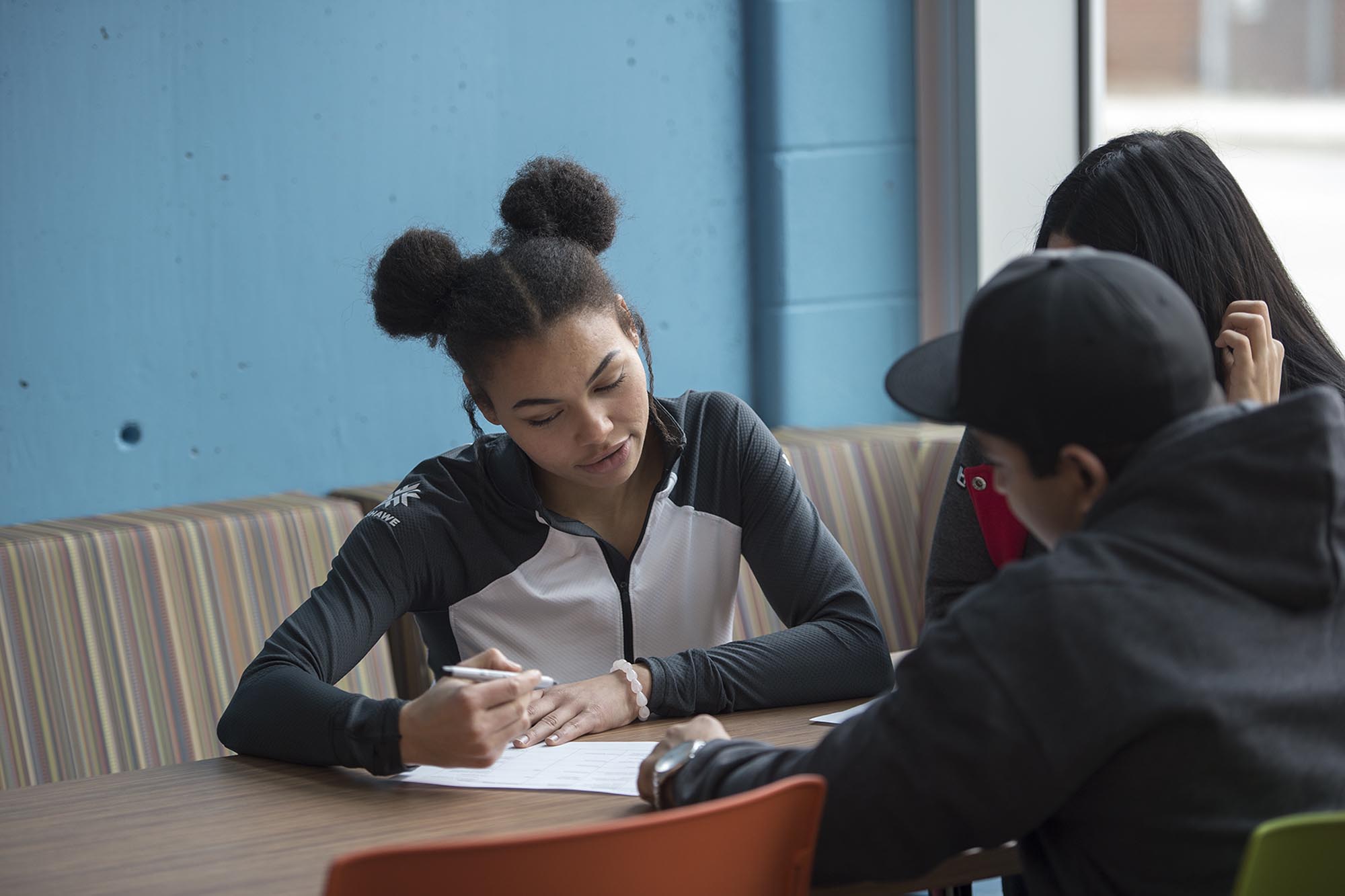 Three students sitting at table talking and filling out form