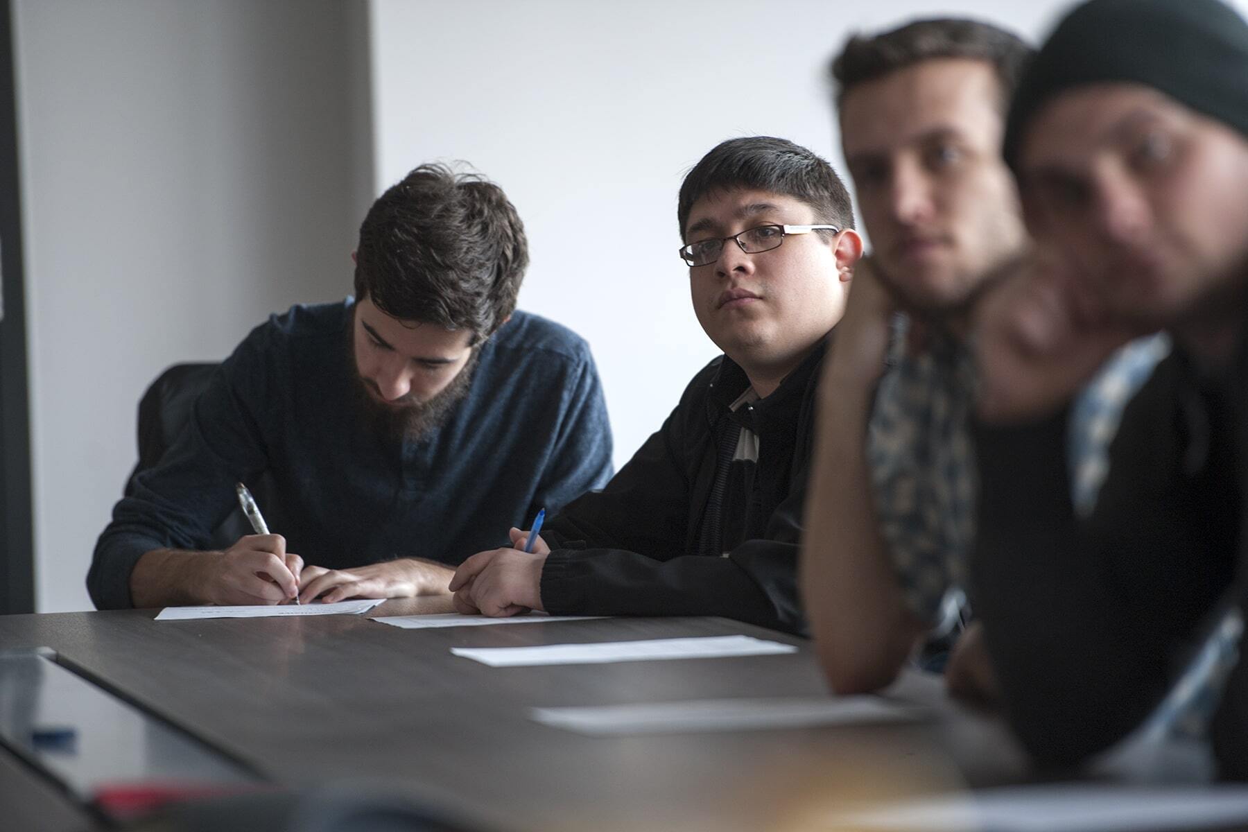 four men sitting at a table and one of them taking notes