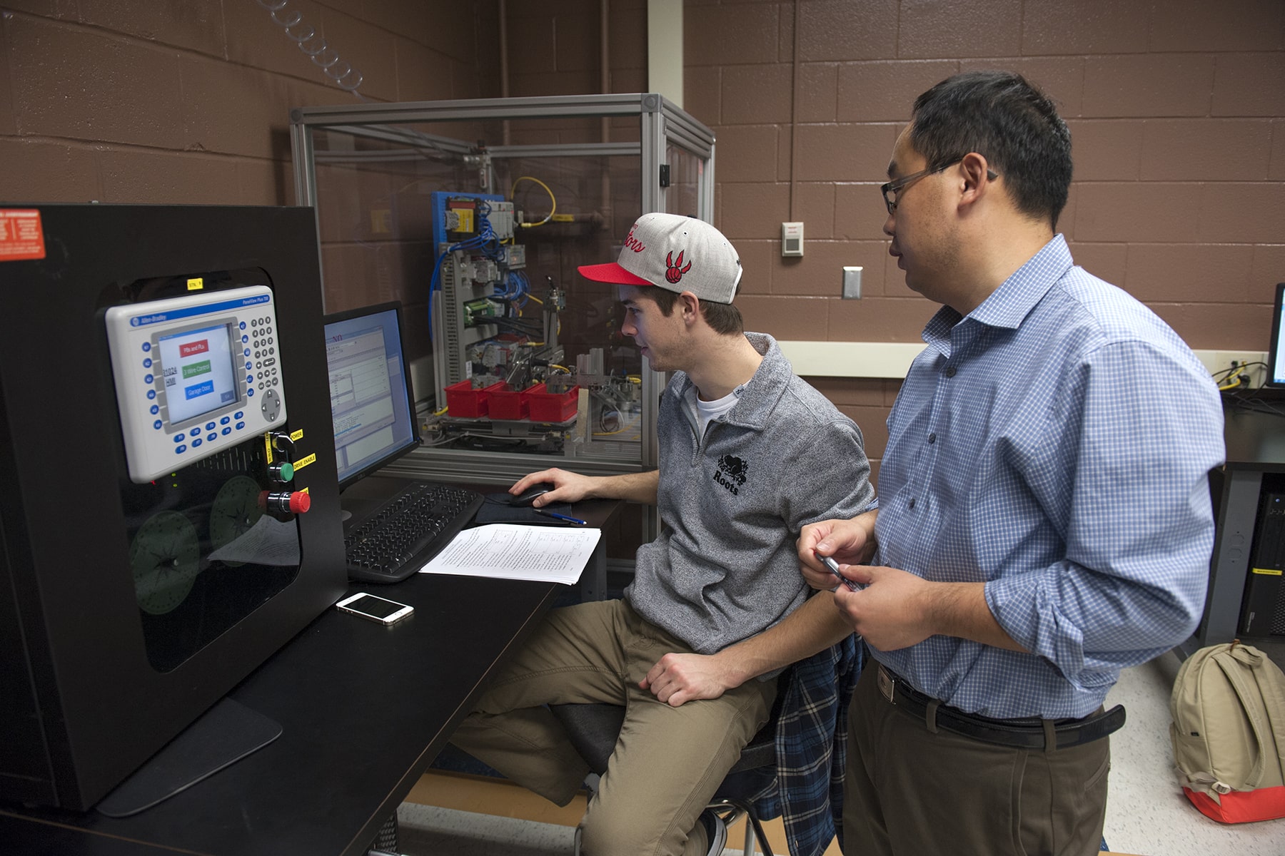 two people in front of electrical equipment and computer