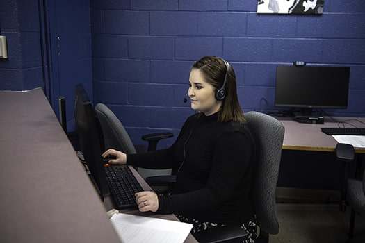 administrative student sits at computer with headset on