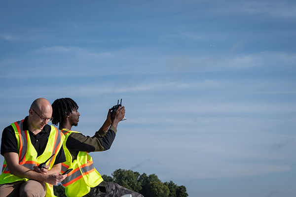 two people in high visibility vests operate drone remotely