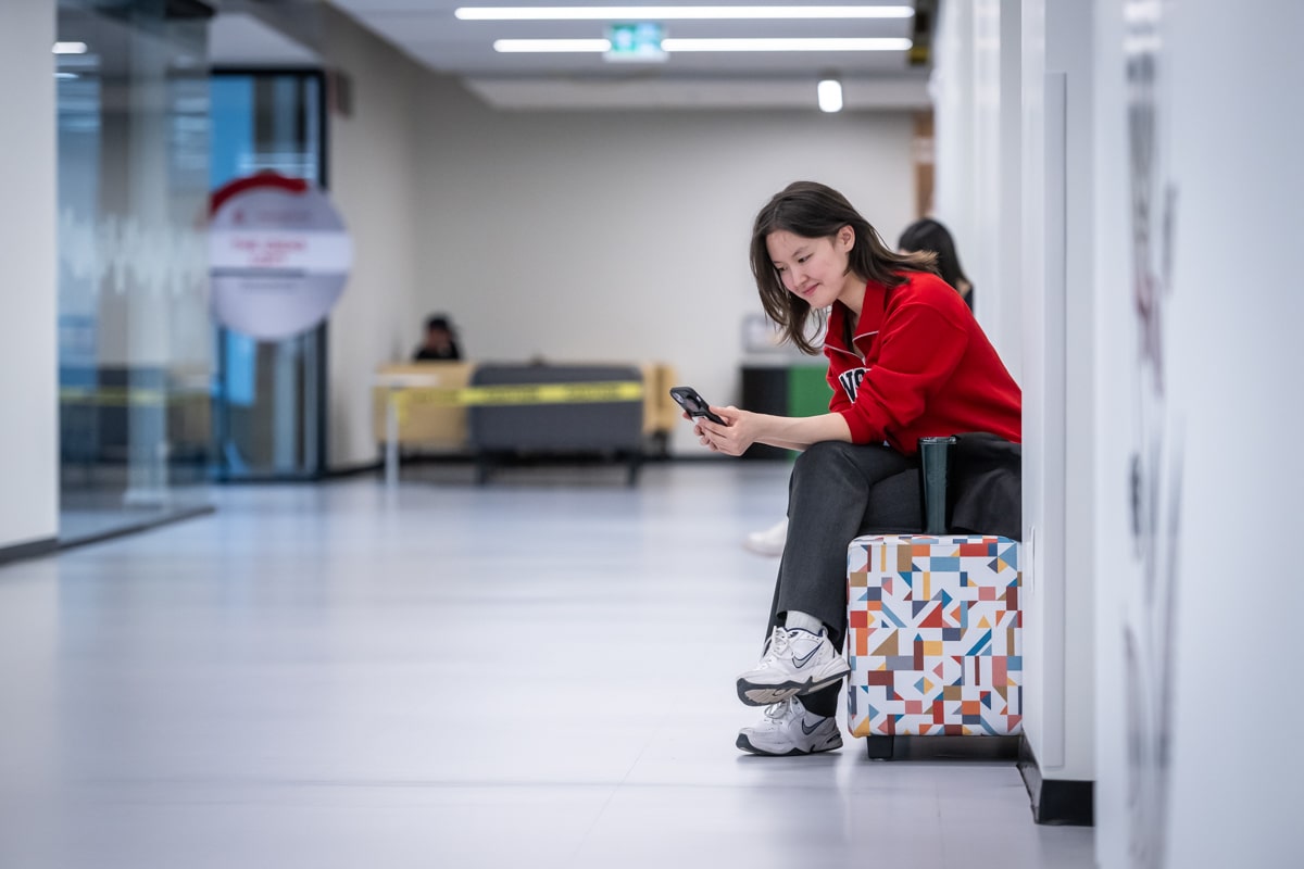 student looks at phone while sitting in college hallway