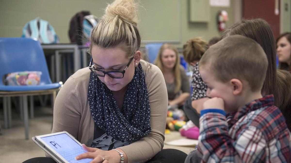 teacher shows young student letters on a tabletq