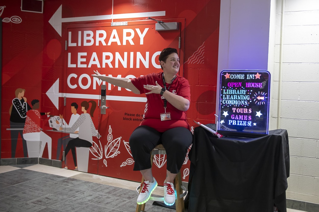 woman motions toward Library Learning Commons doorway at event