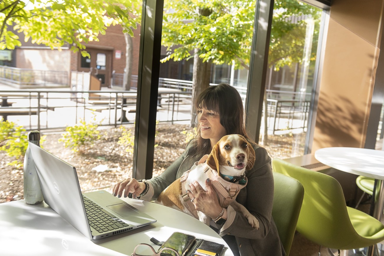 student sits in Fanshawe study area holding dog while working on laptop