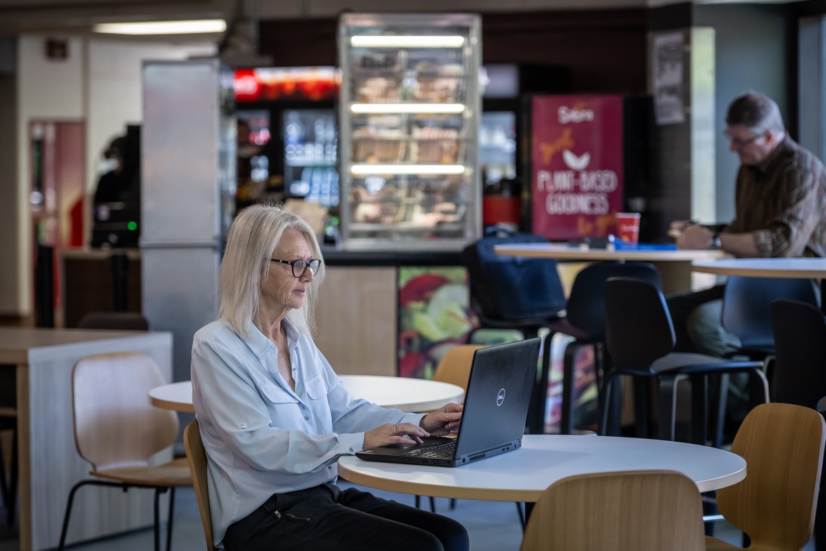 woman sits at table in public space with laptop