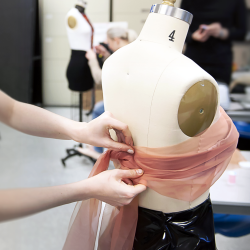 Closeup of student hands pinning sheer fabric to a fashion mannequin.